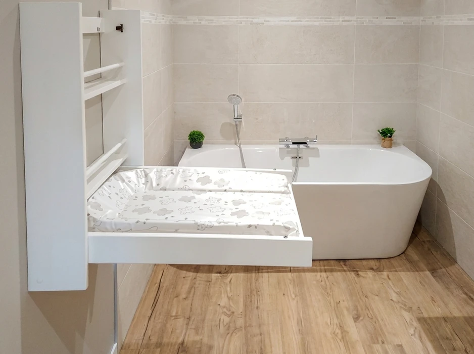 Salle de bain moderne avec baignoire îlot blanche semi-encastrée, robinetterie mitigeur chromée avec douchette, table à langer pliante murale extractible fixée sur radiateur sèche-serviettes blanc