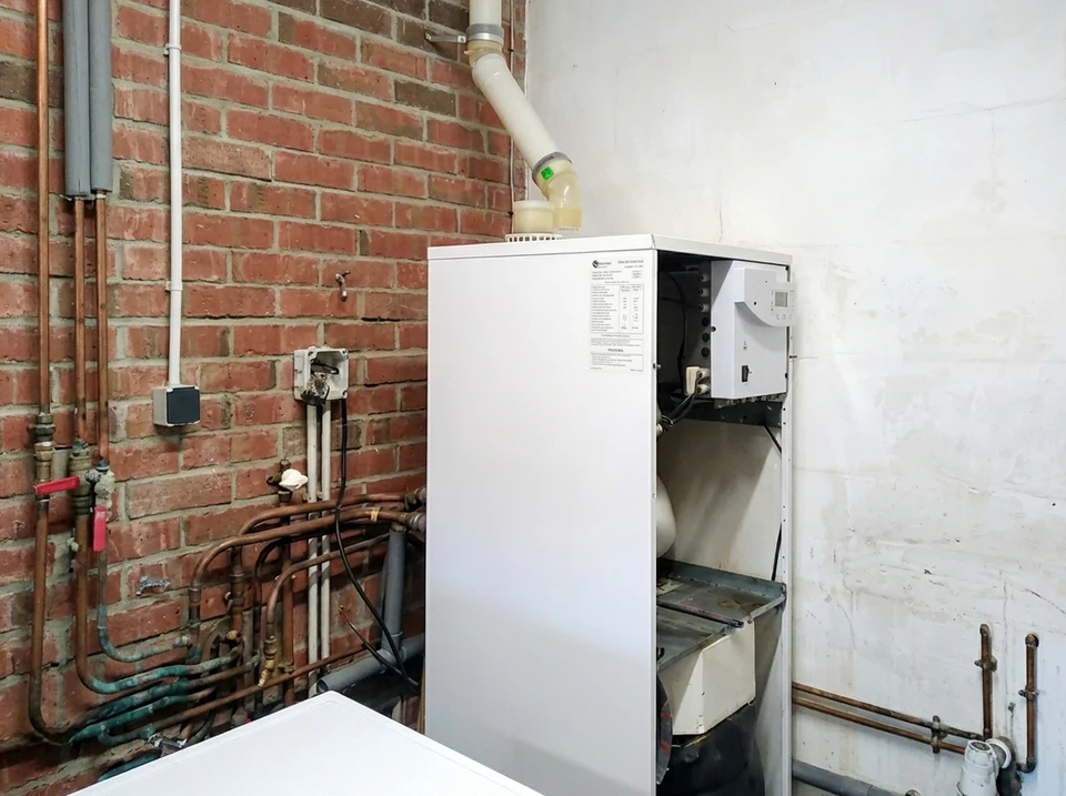 Un technicien en salopette et chemise à carreaux effectue la maintenance d'une chaudière murale domestique dans un local technique