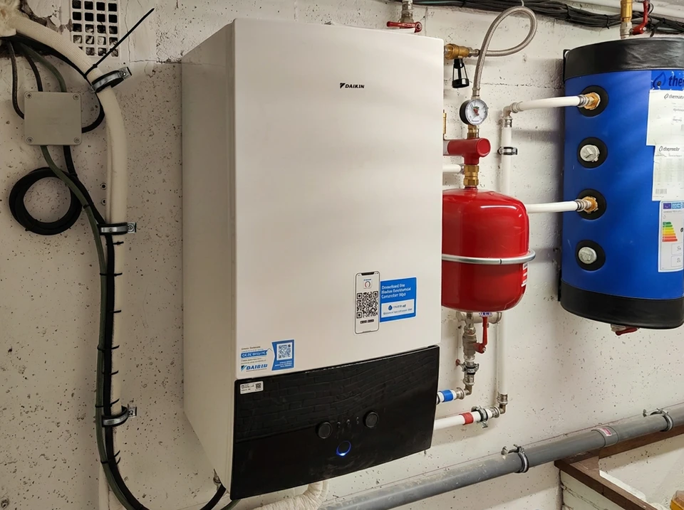 Un technicien en salopette et chemise à carreaux effectue la maintenance d'une chaudière murale domestique dans un local technique