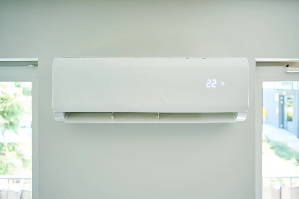 Intérieur moderne avec climatiseur mural blanc en fonctionnement, flux d'air visible soufflant vers des rideaux blancs flottants près d'une fenêtre